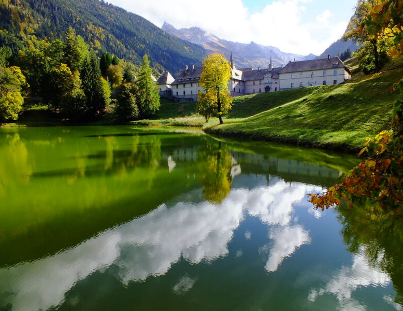Chartreuse du Reposoir en Haute-Savoie entourée de montagnes et de forêts, avec son plan d’eau au premier plan